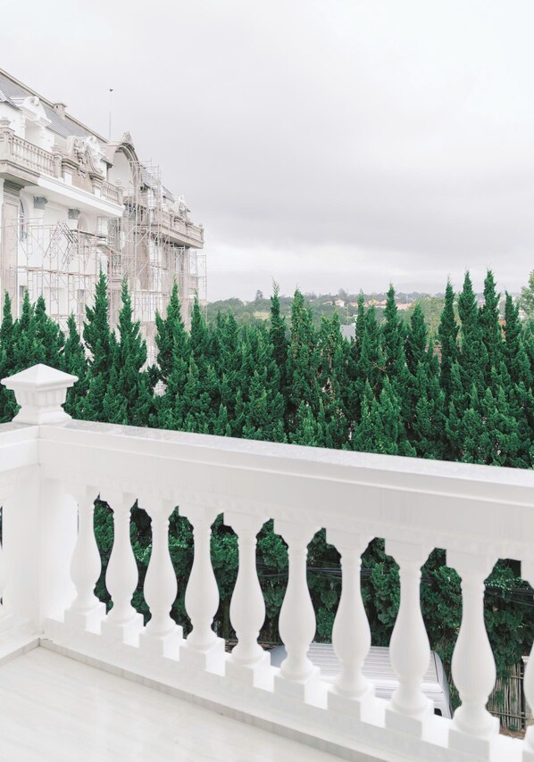 A white balustrade with a view of a building and a row of evergreen trees. - Peach Valley (Da Lat)
