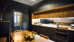 Une cuisine moderne avec des meubles de couleur sombre, un plan de travail en bois et un saladier de fruits posé sur la table.