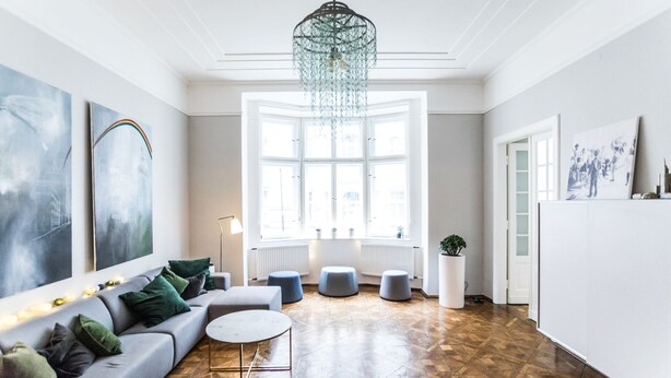 Un salon spacieux avec une grande fenêtre, un canapé gris, une table basse ronde et un lustre.