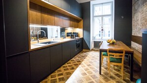 Une cuisine moderne avec des meubles de couleur sombre, un plan de travail en bois et un coin repas comprenant une table et des chaises.