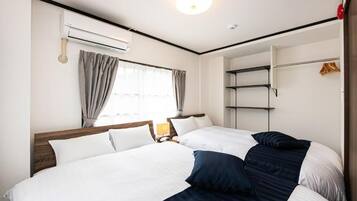 Een hotelkamer met twee bedden, een kledingkast, een raam met gordijnen, een airconditioning en een bedlamp.