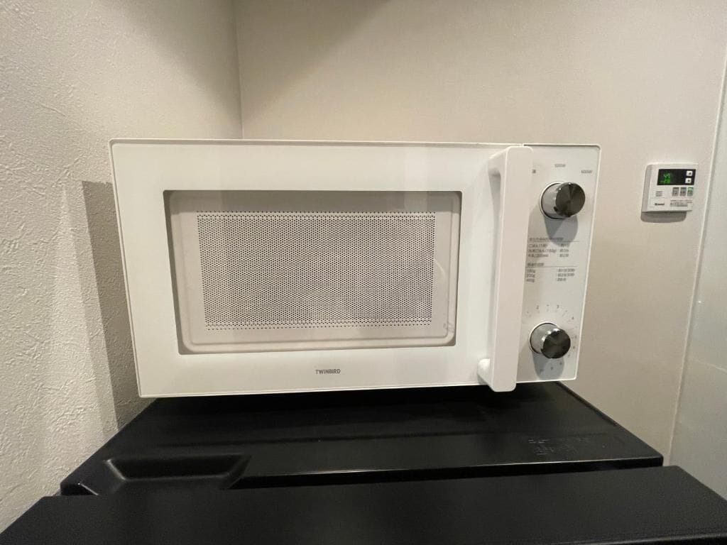 Eine weiße Mikrowelle mit digitalem Display und Bedienelementen, auf einer schwarzen Arbeitsplatte platziert.