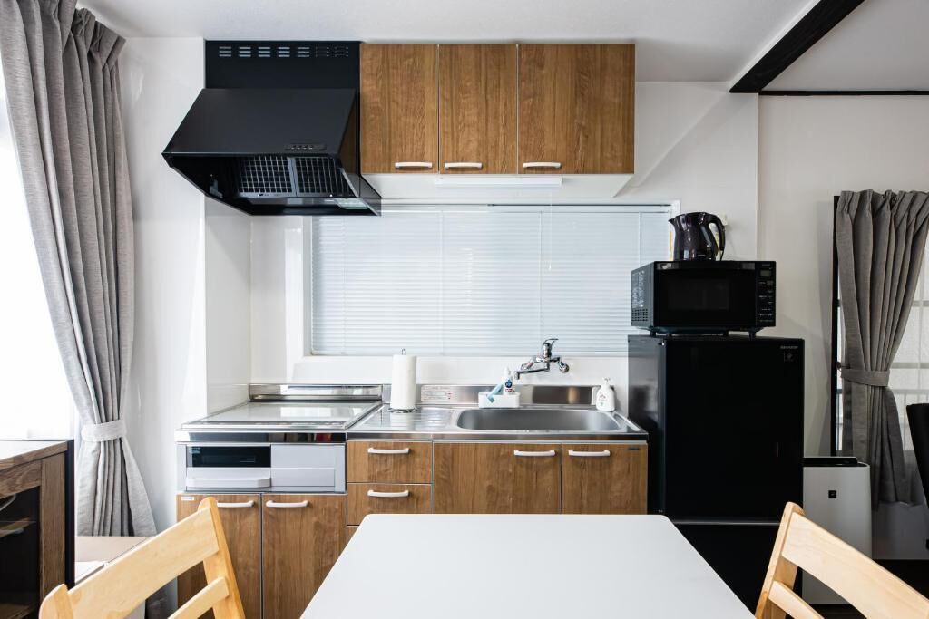 Una cocina compacta con armarios de madera, una campana extractora negra, un microondas y un fregadero.