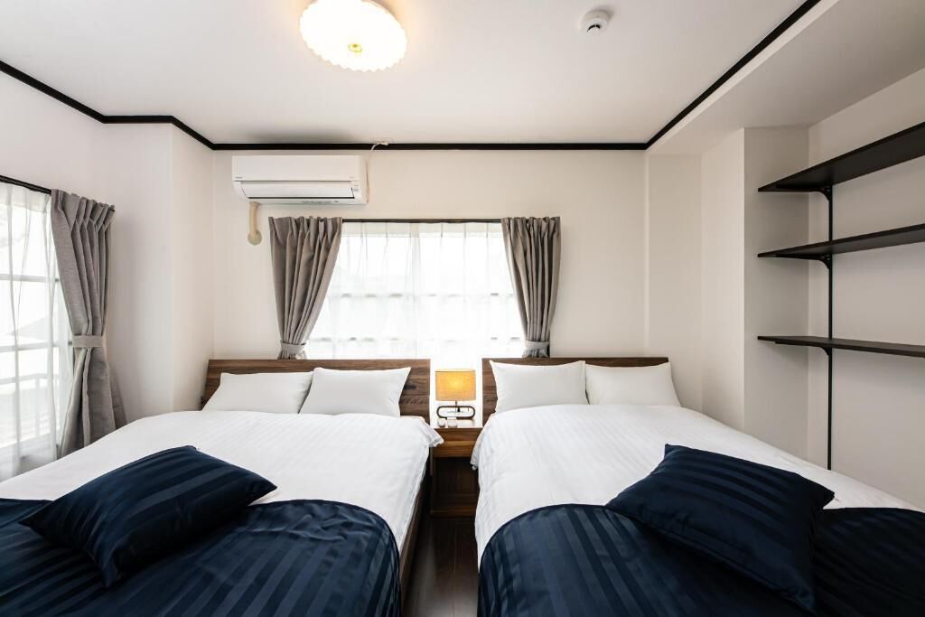Habitación de hotel con dos camas, una mesita de noche, un equipo de aire acondicionado y una ventana con cortinas.