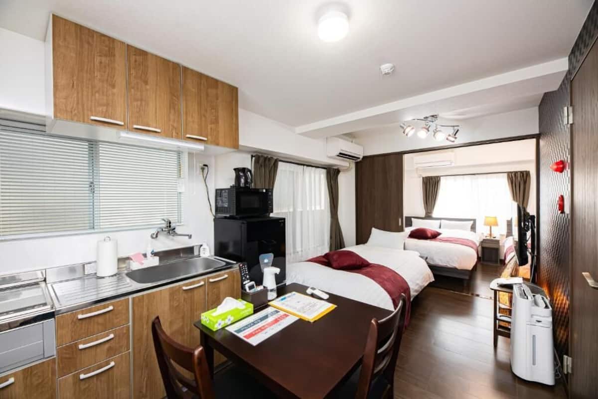 A compact hotel room with a kitchenette, a bed, a bedside table, and a bathroom.