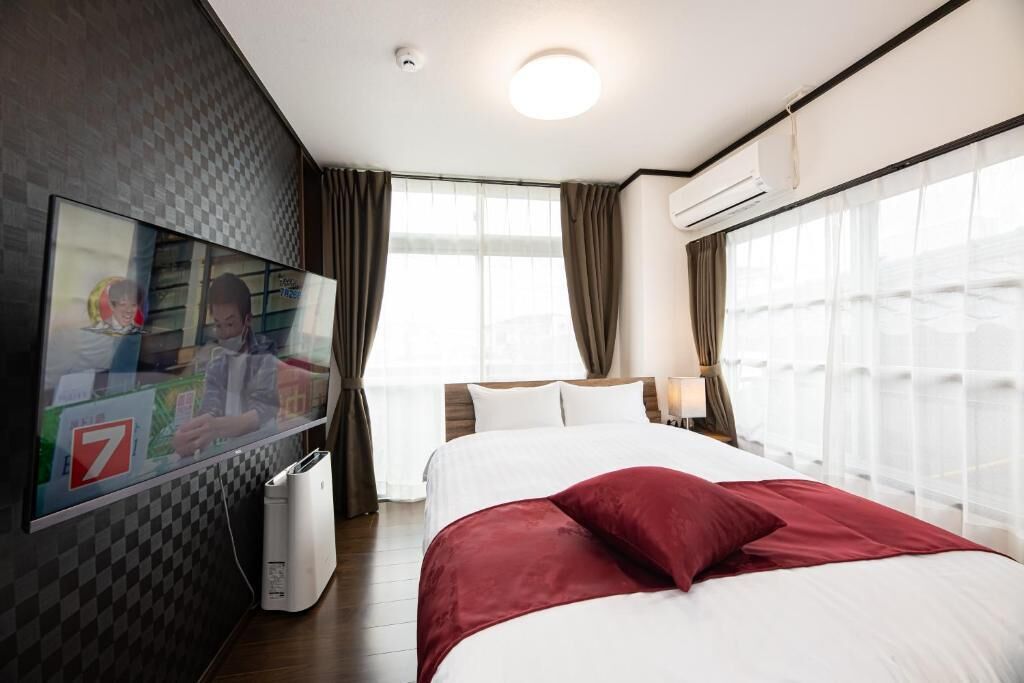 Habitació d'hotel amb un llit, una televisió penjada a la paret i una finestra amb cortines.