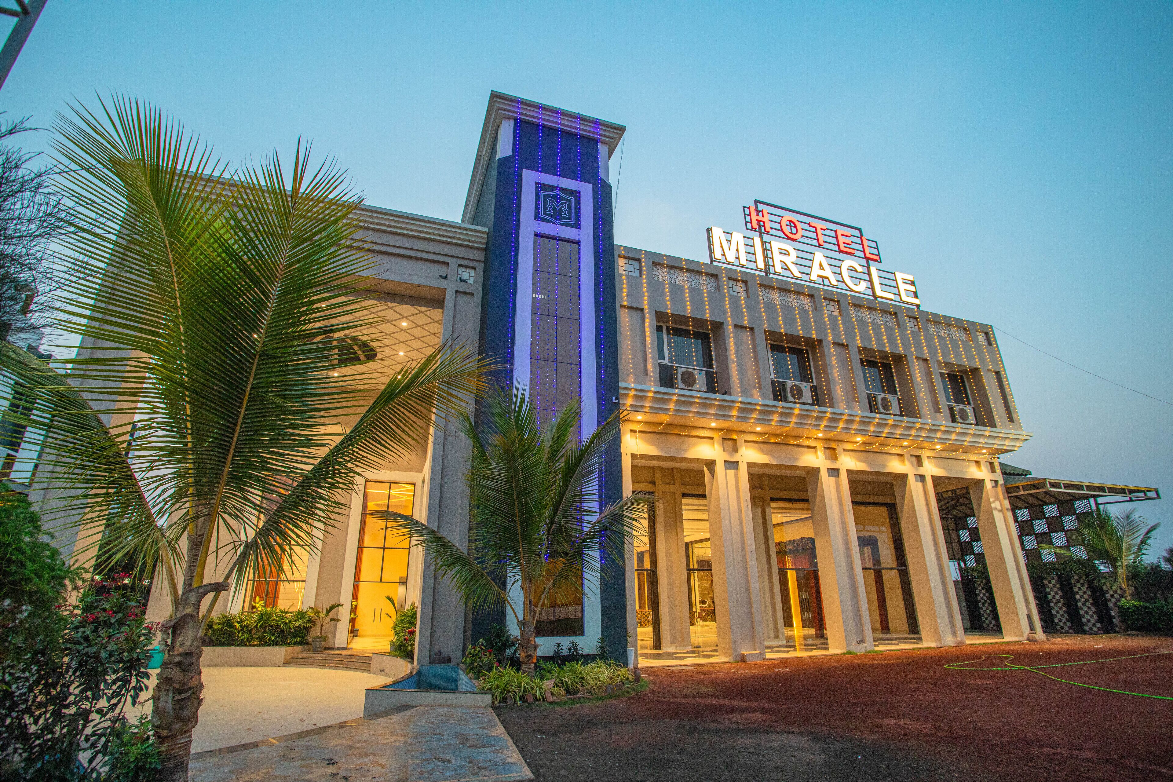 A hotel with a prominent sign reading "HOTEL MIRACLE." It features a modern facade with large windows and a symmetrical entrance.