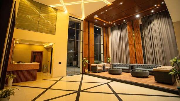 A modern lobby with a reception desk, seating area, and large windows. - Hotel Miracle  (Ujjain)