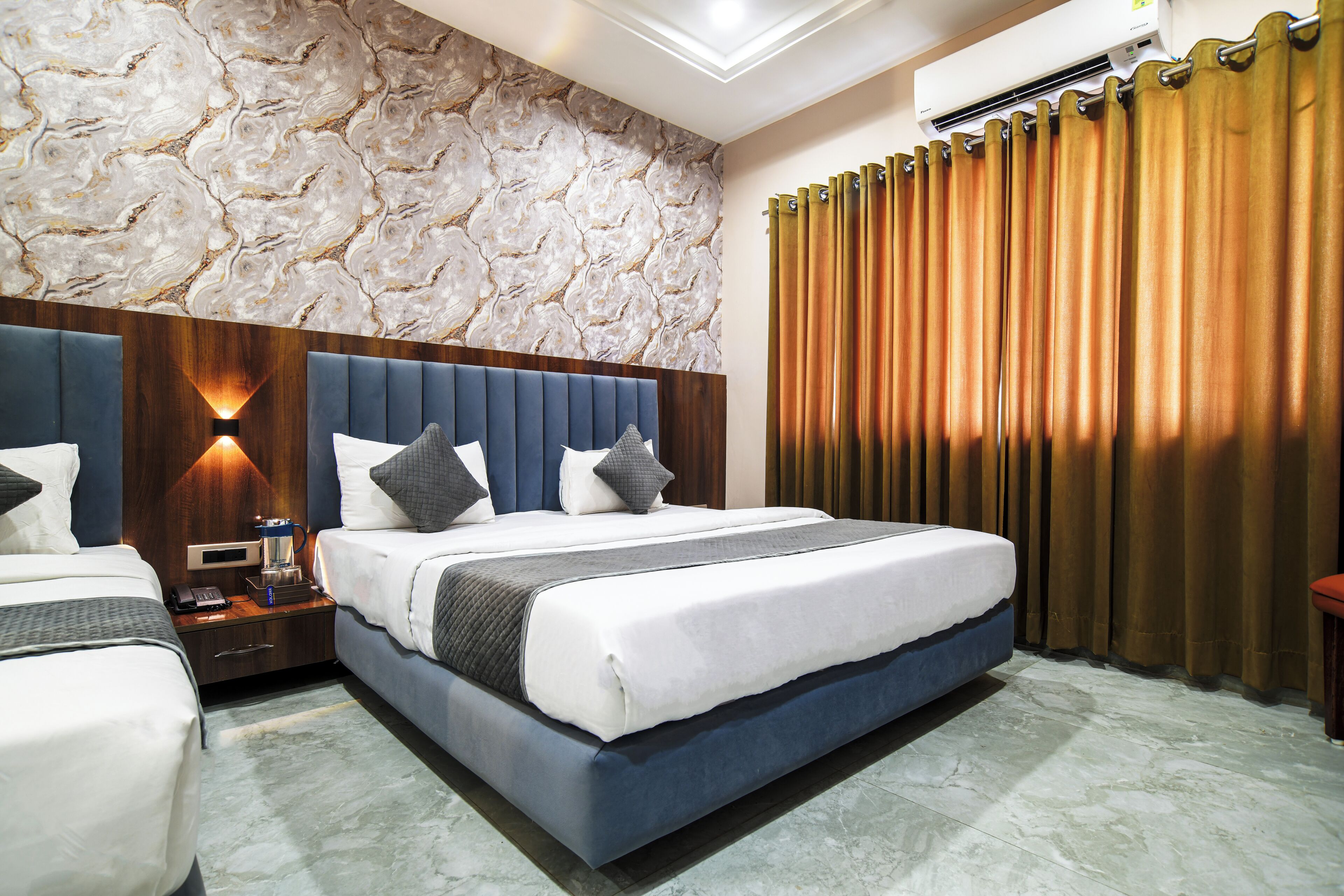 A hotel room with a large bed, a nightstand, a wall-mounted air conditioner, and a curtain.