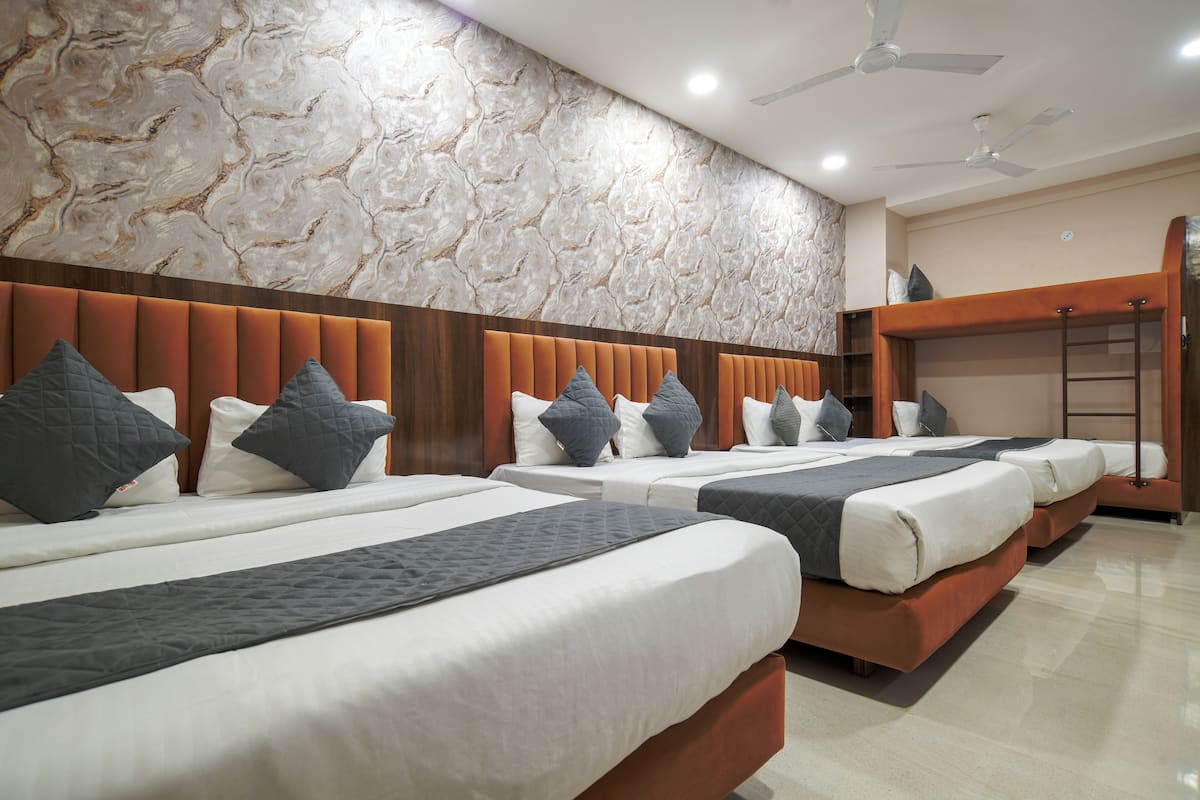 A hotel room with four beds arranged in a row, a ceiling fan, and a stone-patterned wall.