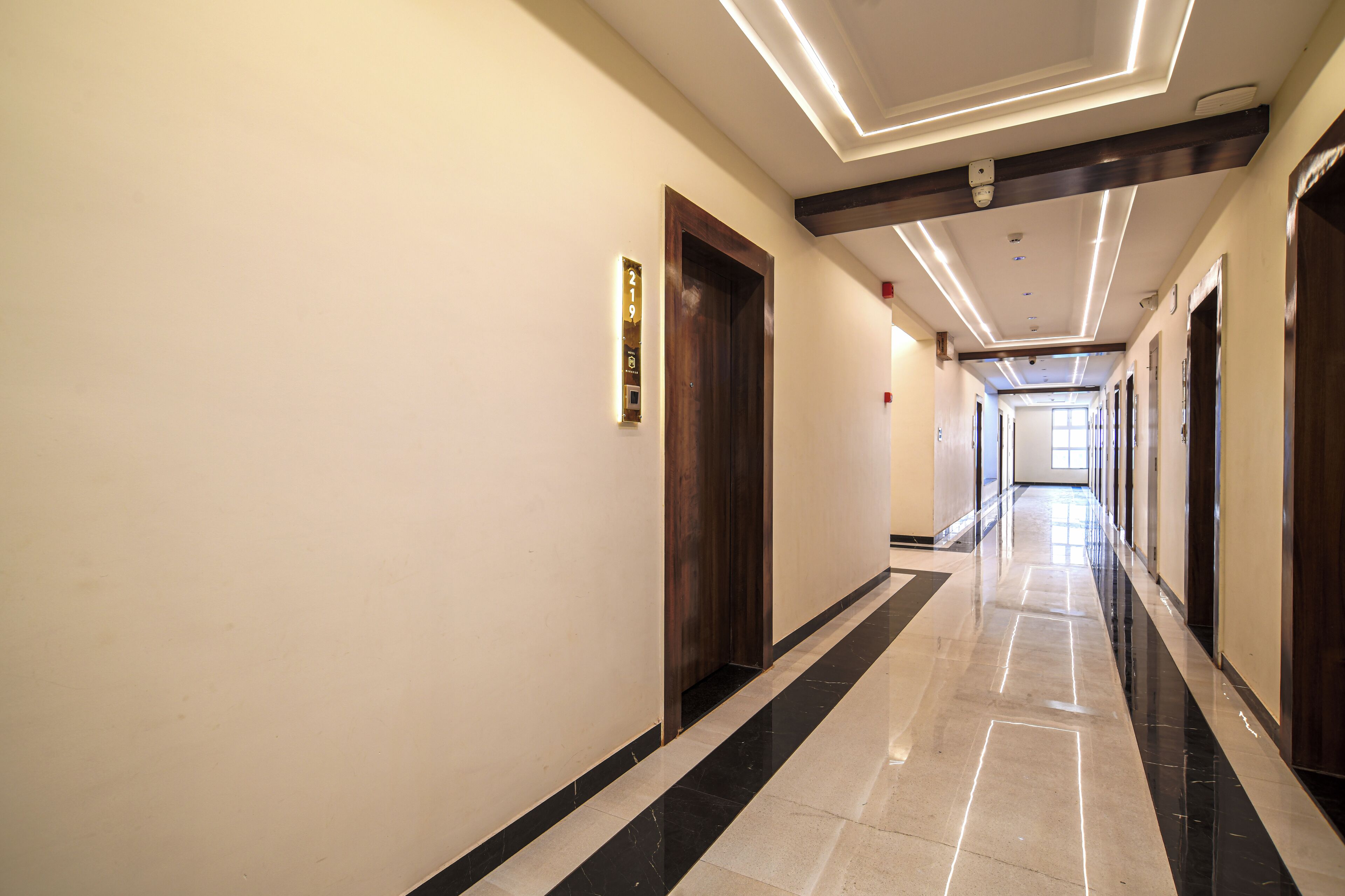 A long, well-lit hallway with a polished floor, wooden doors, and a modern ceiling design.