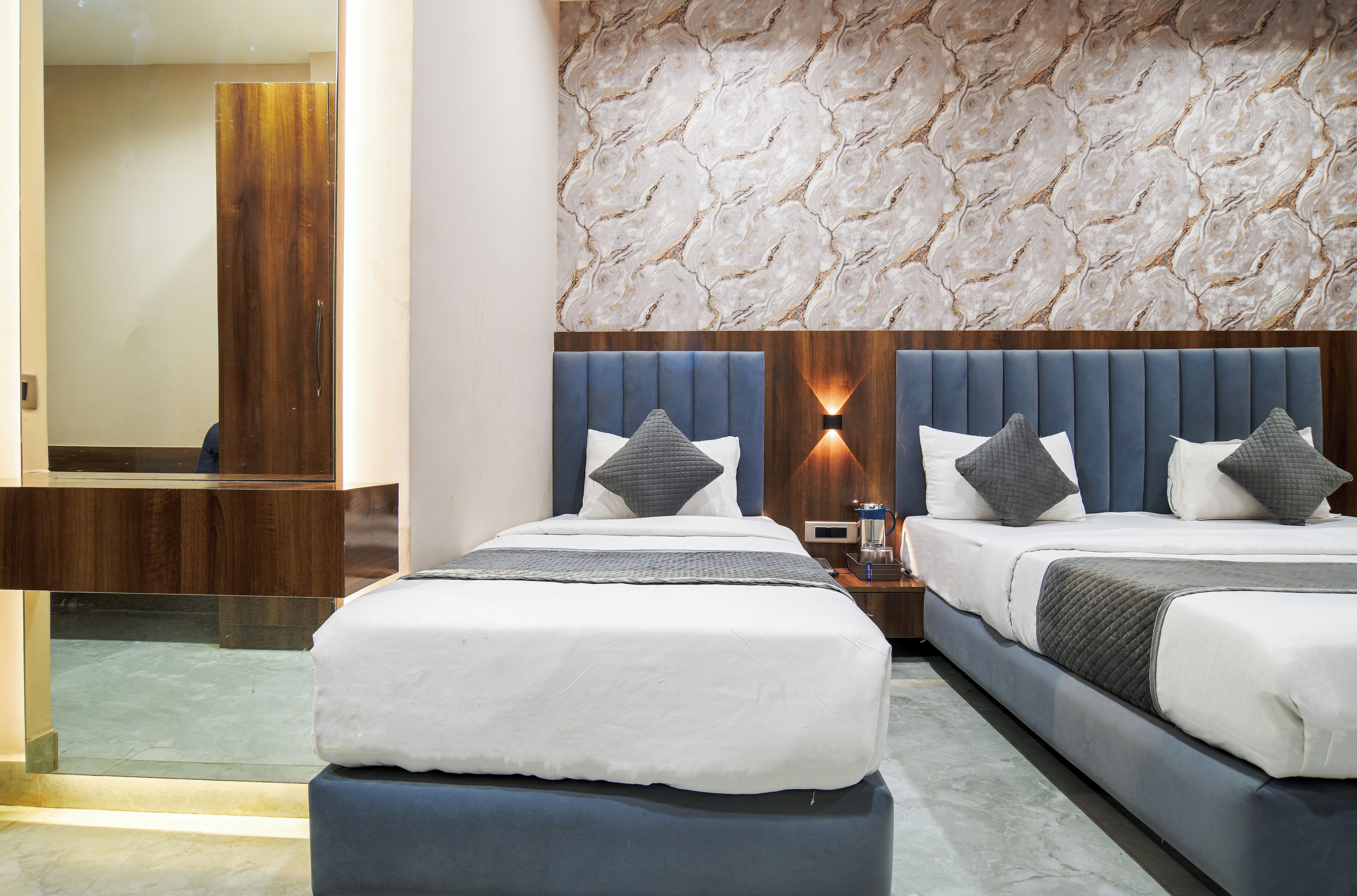 A modern hotel room with two beds, a marble-patterned wall, and a wooden accent wall.