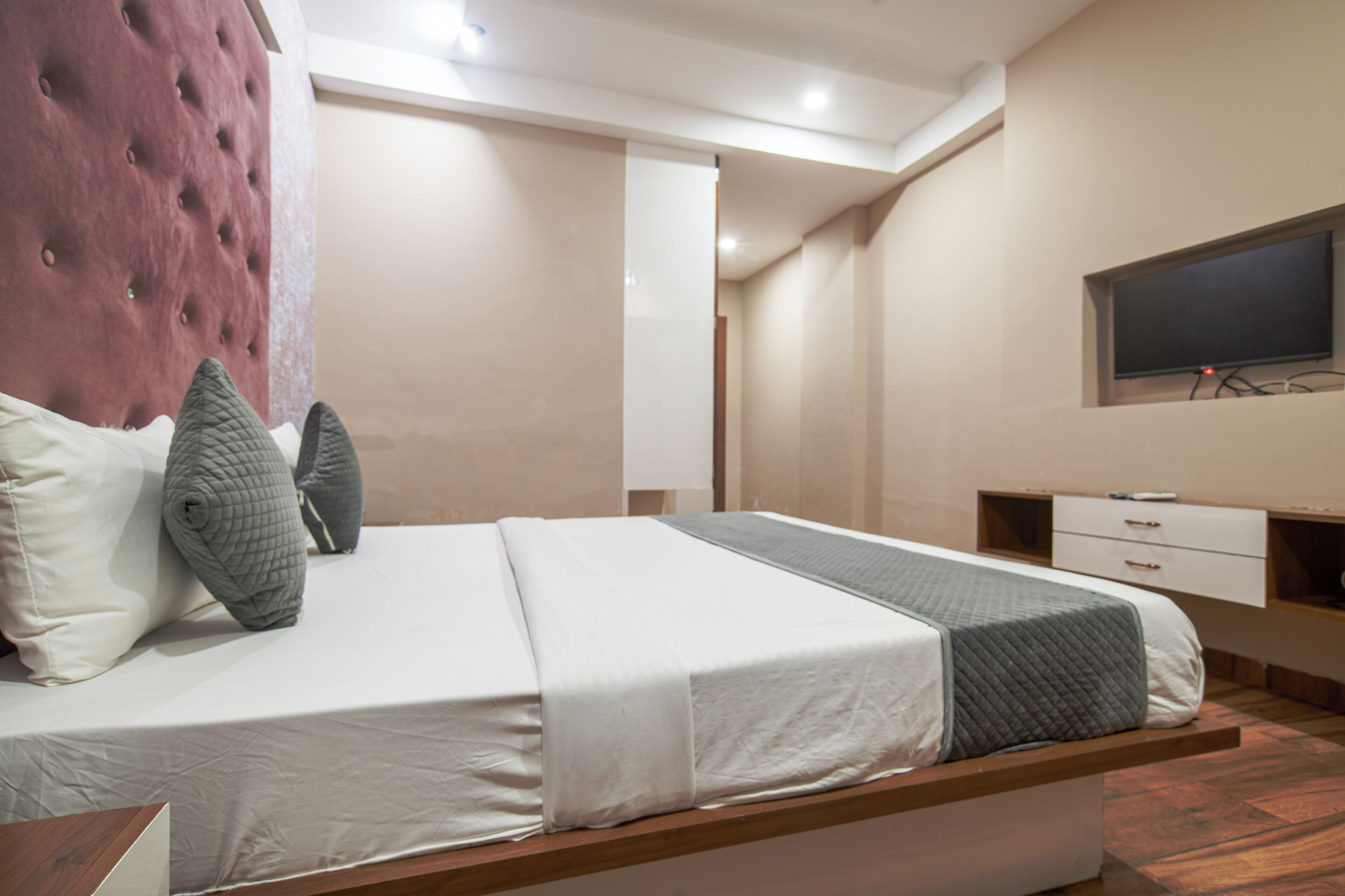 A modern bedroom with a bed, pillows, a TV, and a wooden nightstand.