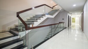 A modern staircase with glass railings and wooden handrails, leading to an upper floor. - Hotel Miracle  (Ujjain)