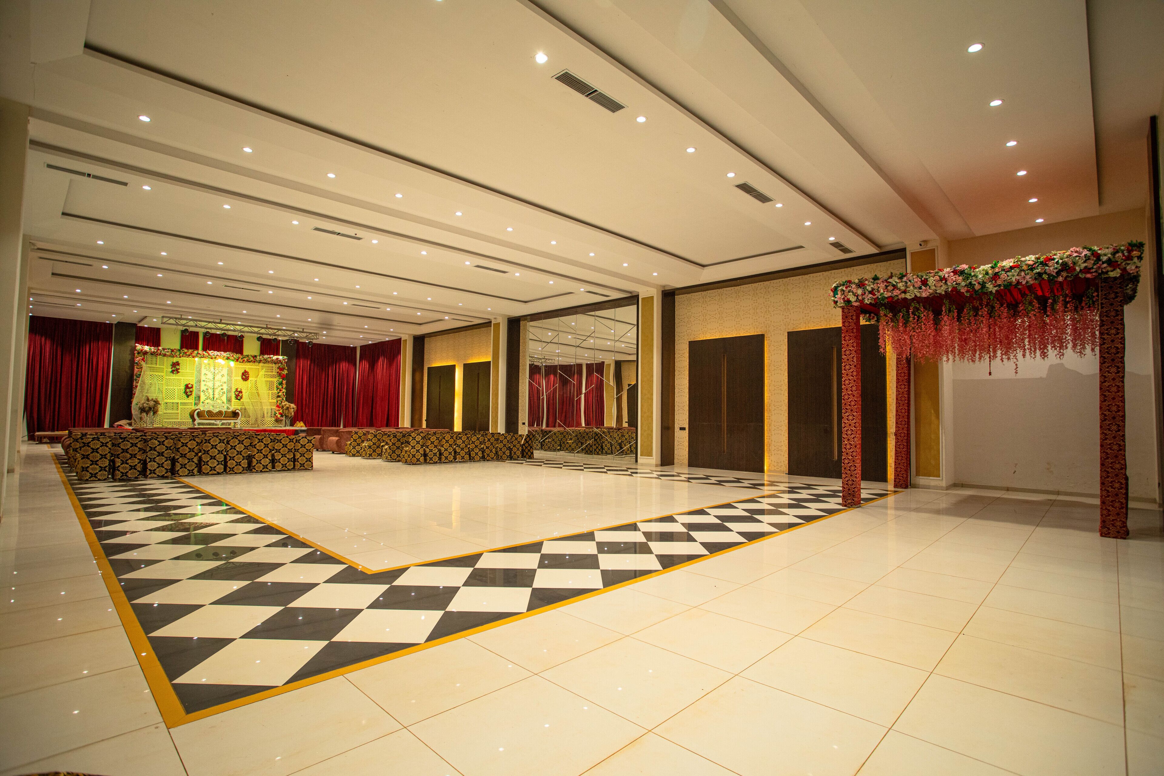 A spacious hall with a checkered floor, a stage with red curtains, and a floral decoration.