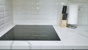 A kitchen with white subway tiles, a black induction cooktop, and a wooden knife block with knives. - Molivu Homes 1BR | New Build | Pet Friendly | W/D (San Jose)