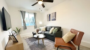 A modern living room with a sofa, a coffee table, a TV, and a ceiling fan. - Molivu Homes 1BR | New Build | Pet Friendly | W/D (San Jose)