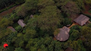 An aerial view of a rural area with several traditional thatched-roof houses surrounded by dense vegetation. - Ishara Lodge (Arusha)