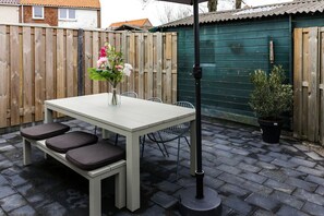 Relax on the patio with a light table and comfortable benches, surrounded by lush greenery and a beautiful vase with fresh flowers.