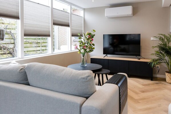 Relax in this inviting living space with a comfortable sofa, flat-screen TV, and a beautiful vase with flowers.