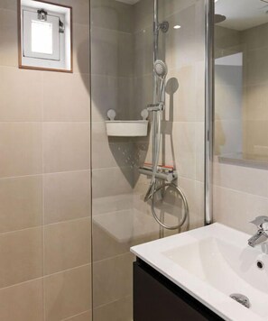 Bathroom features a glass-enclosed shower, sink with handheld showerhead and wall-mounted faucet.