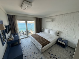 Habitación de hotel con cama, escritorio, silla, televisión y vista al mar.