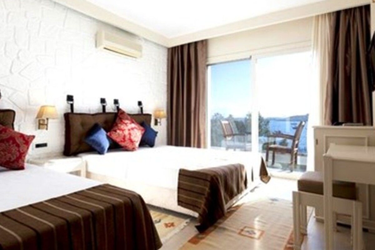 A hotel room with a bed, bedside tables, a desk, and a view of the outdoors.