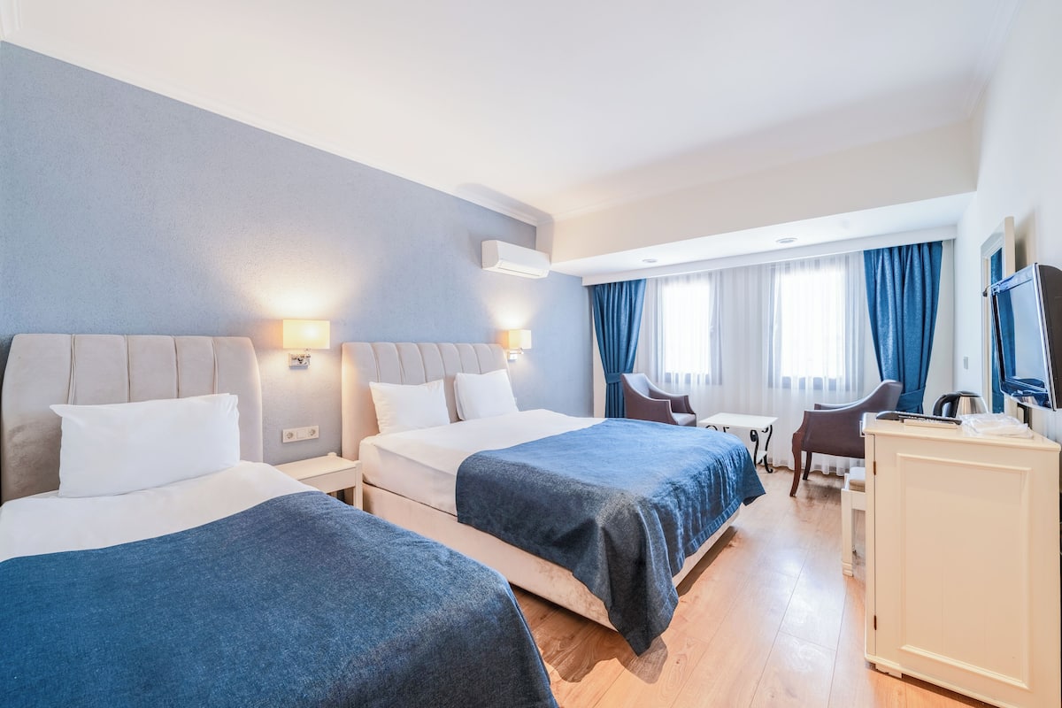 A hotel room with two beds, a desk, a chair, a TV, and a wardrobe.