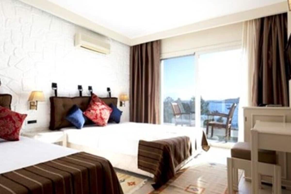 A hotel room with a bed, bedside tables, a desk, and a view of the outdoors.