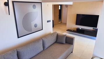 Una sala de estar moderna con un sofá gris, una obra de arte abstracto enmarcada, un televisor de pantalla plana y una mesita auxiliar pequeña.