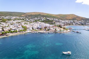 Un pueblo costero con un puerto deportivo, edificios y un paisaje montañoso al fondo.