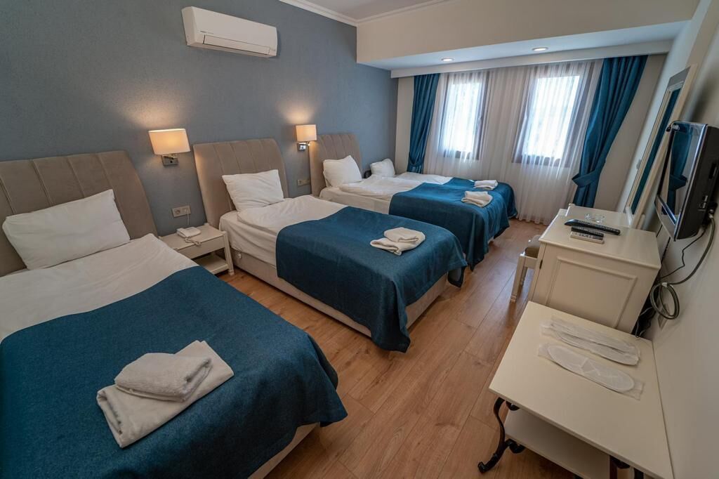 Une chambre d’hôtel avec trois lits, un bureau avec une télévision et une fenêtre avec des rideaux.