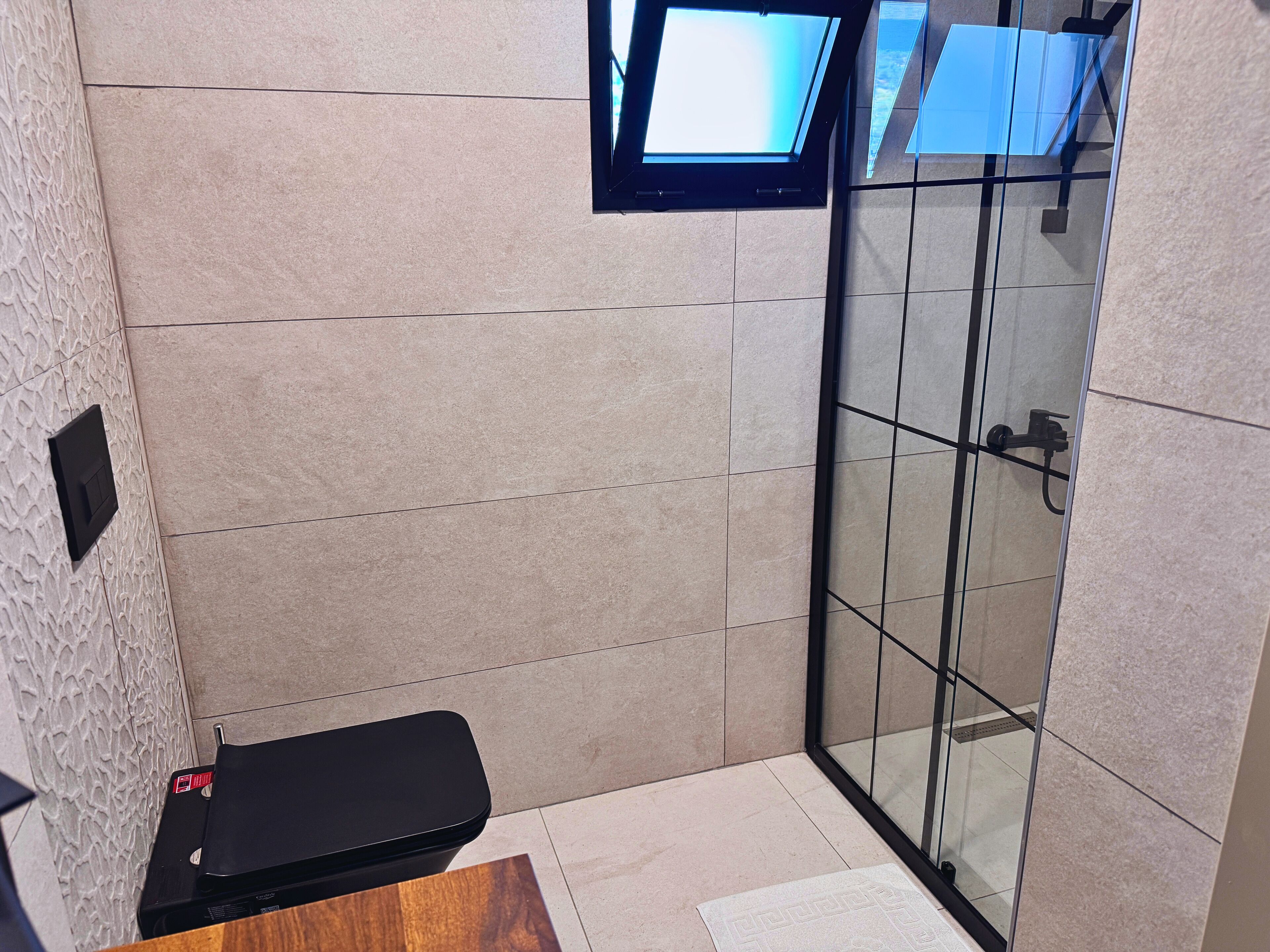 A modern bathroom with a glass shower enclosure, a black bench, and a mounted television.