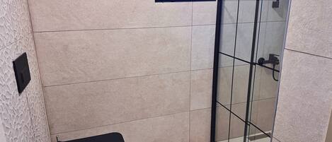 A modern bathroom with a glass shower enclosure, a black bench, and a mounted television.