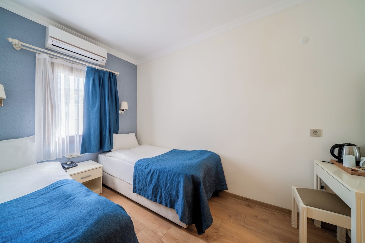 A hotel room with two beds, a desk, a chair, a coffee maker, and an air conditioning unit.