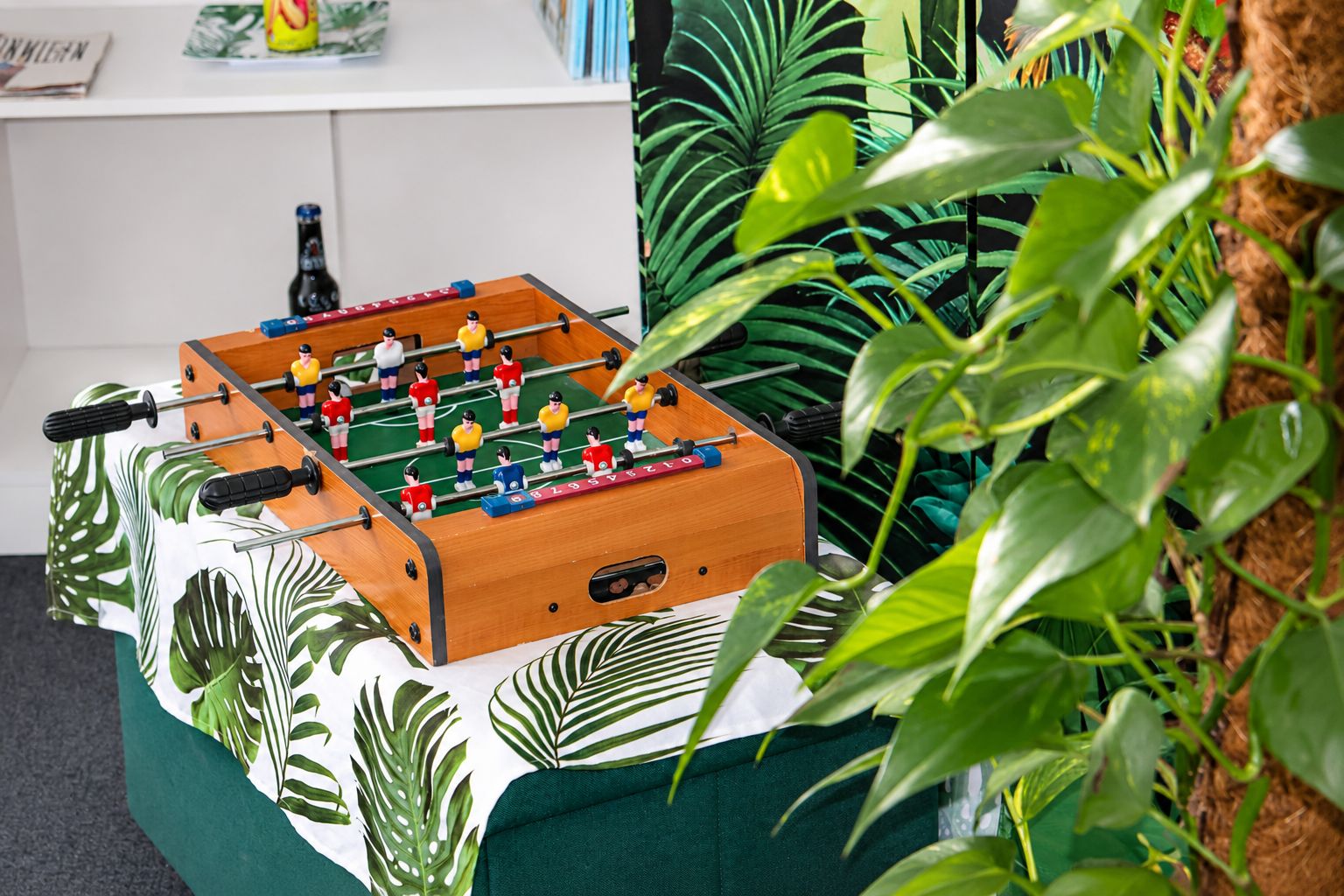 Une table de baby-foot dans une pièce avec un canapé vert et des plantes tropicales.