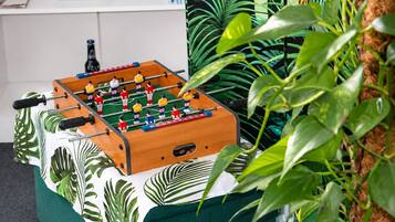 Une table de baby-foot dans une pièce avec un canapé vert et des plantes tropicales.