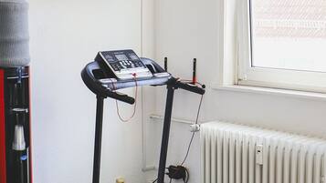 Ein Zimmer mit Laufband, Wandfernseher, Heizkörper und Fenster mit Blick auf Gebäude.