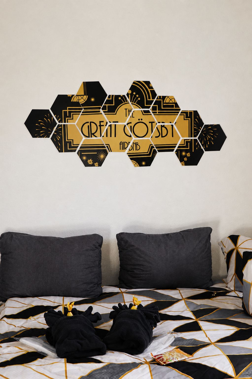 Une chambre avec une couvre-lit à motifs géométriques, deux oreillers et une décoration murale présentant un motif hexagonal et du texte.