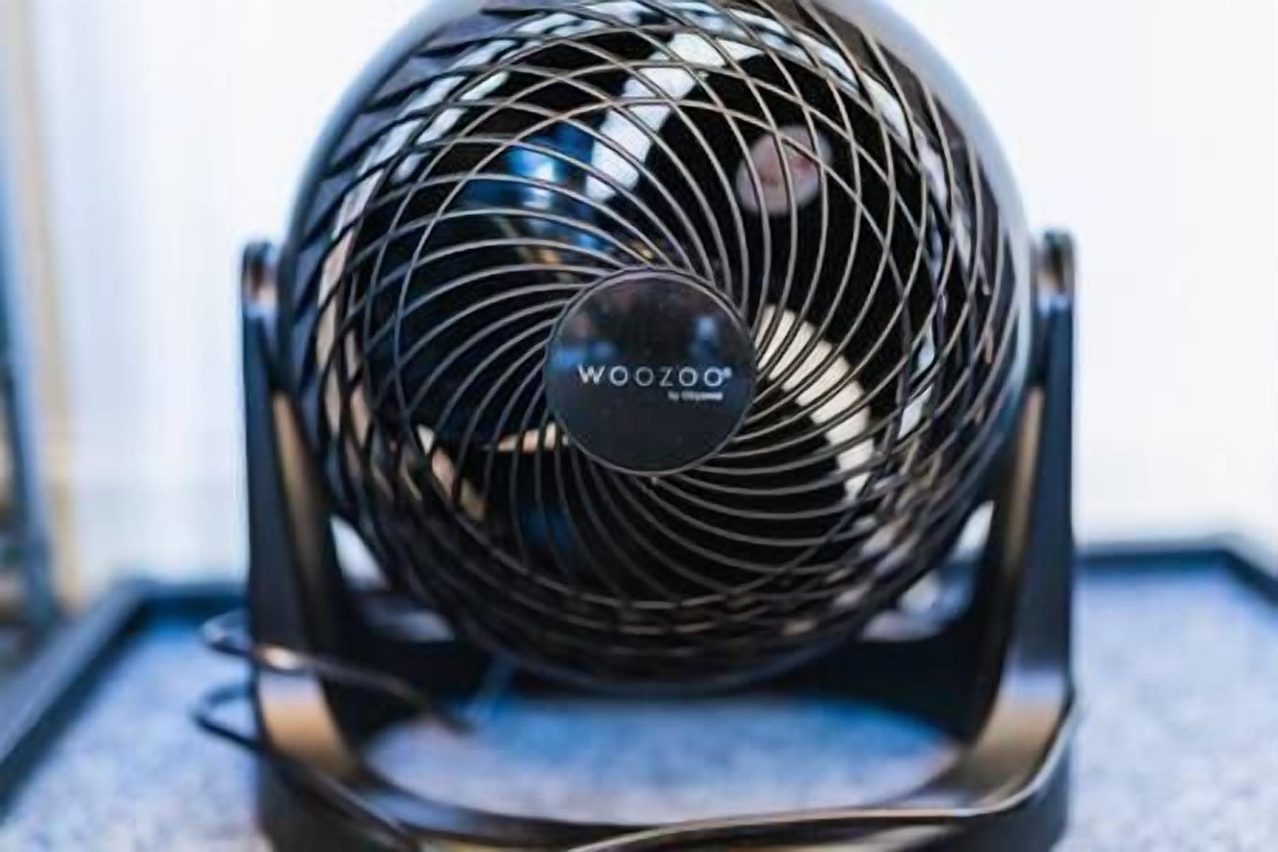 En sort, bærbar ventilator med et cirkulært gitter og mærket "WooZoo" synligt på forsiden.