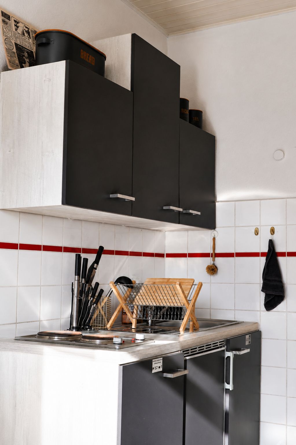 Una cocina con un armario negro, un lavamanos de acero inoxidable y una tabla de cortar de madera.