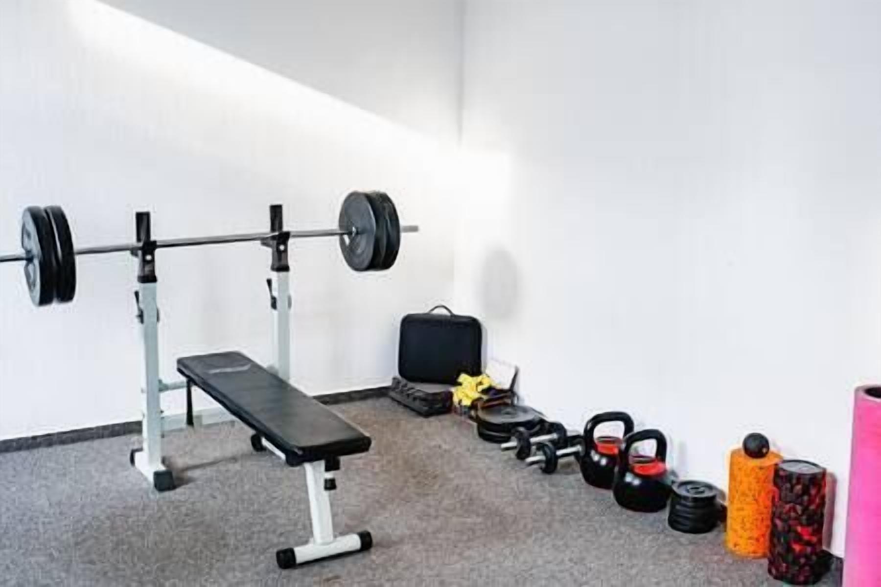 Ein Fitnessraum mit einer Bank, einer Langhantel, Kettlebells und Kurzhanteln.
