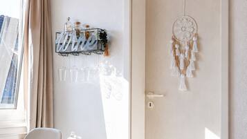 Une pièce avec un plafond en bois, une porte blanche ornée d’un attrape-rêves, un porte-bouteilles fixé au mur et une chaise blanche.