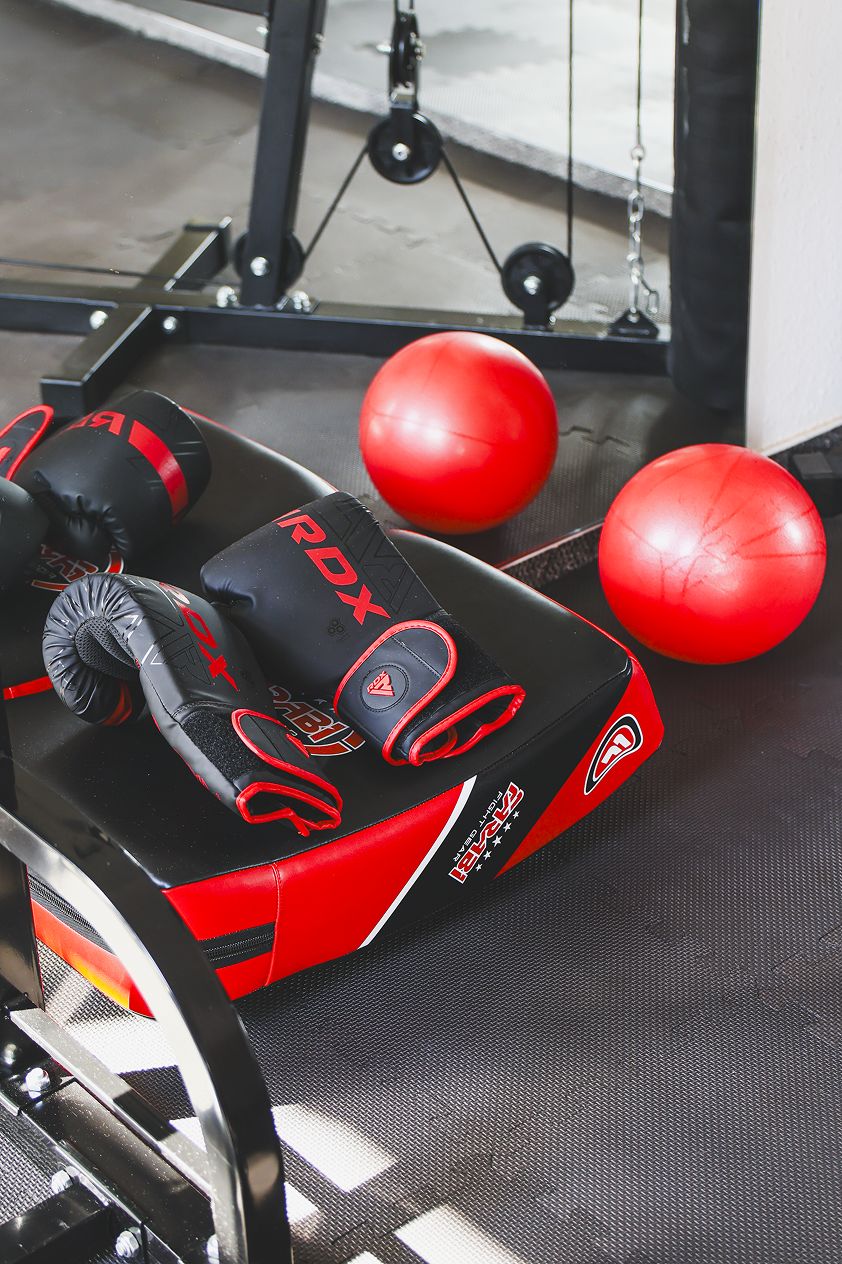 A gym with exercise equipment, including a red and black punching bag, a red exercise ball, and a black weight bench.