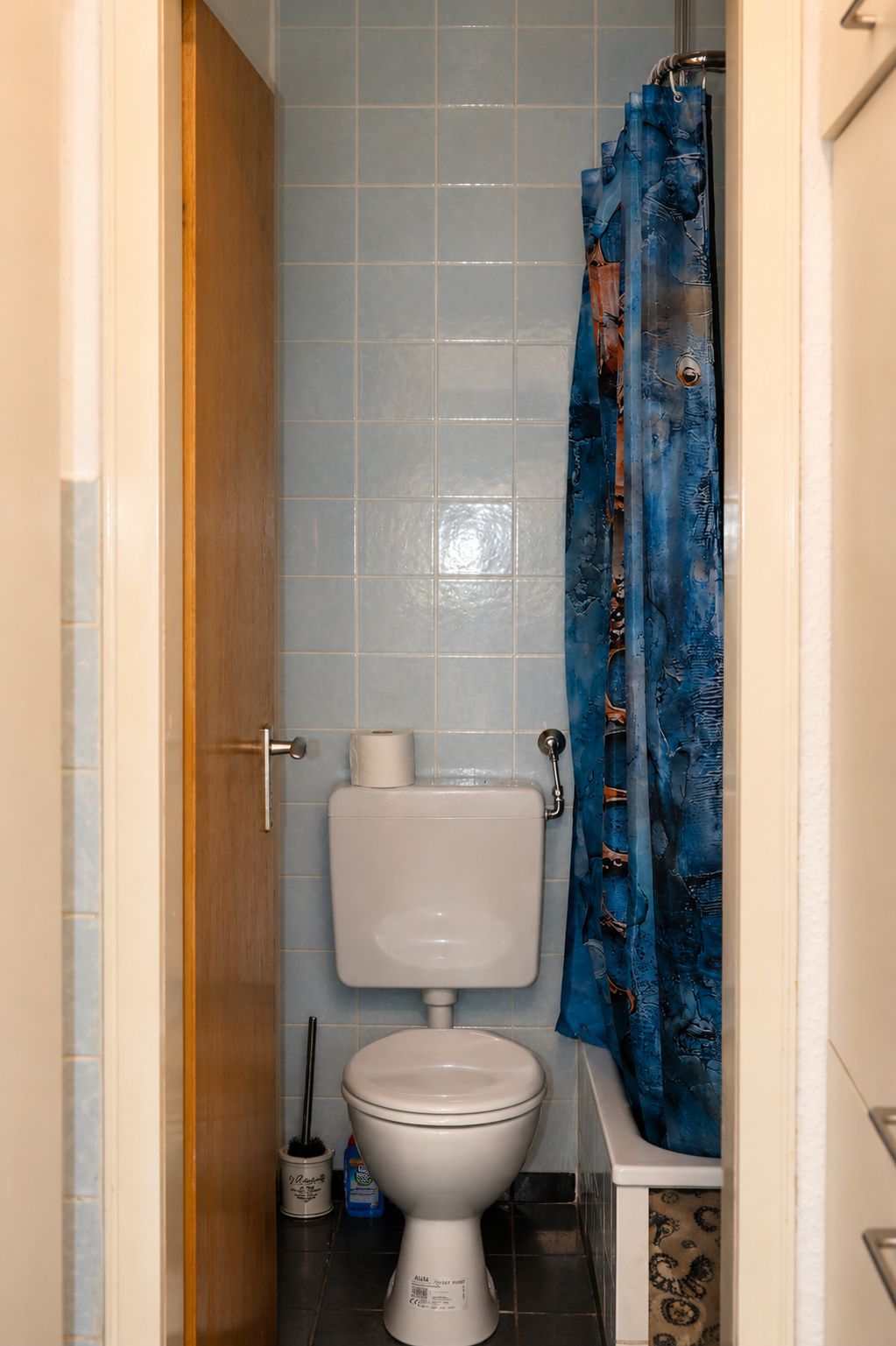 Un baño con inodoro, un rollo de papel higiénico y una cortina de ducha azul.
