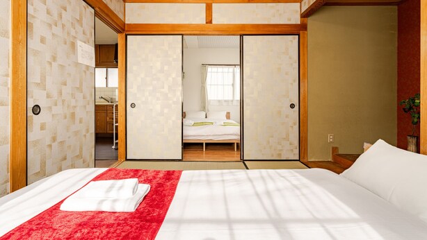 Ein Hotelzimmer mit einem Bett, einem roten Teppich als Farbtupfer und einer Schiebetür zu einem Badezimmer.