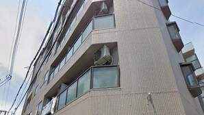 Ein mehrstöckiges Gebäude mit modernem Design, mit einer Schaufensterfront und einer schwarzen Markise sowie einer Bank davor.