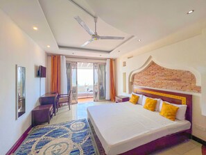 Une chambre d’hôtel avec un grand lit, un bureau, une chaise et un ventilateur de plafond.