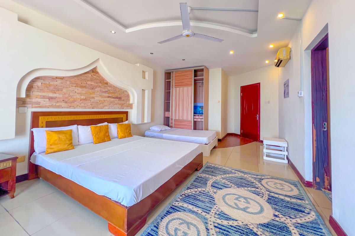 A hotel room with a large bed, a smaller bed, a ceiling fan, a red door, and a patterned rug.