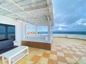 Un espace extérieur abrité, avec vue sur la mer, un banc blanc et un sol carrelé.